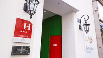 A hotel entrance with a red door, a sign with a white 'H' and three stars, and a sign indicating 'Hotel' and 'Business Center'.