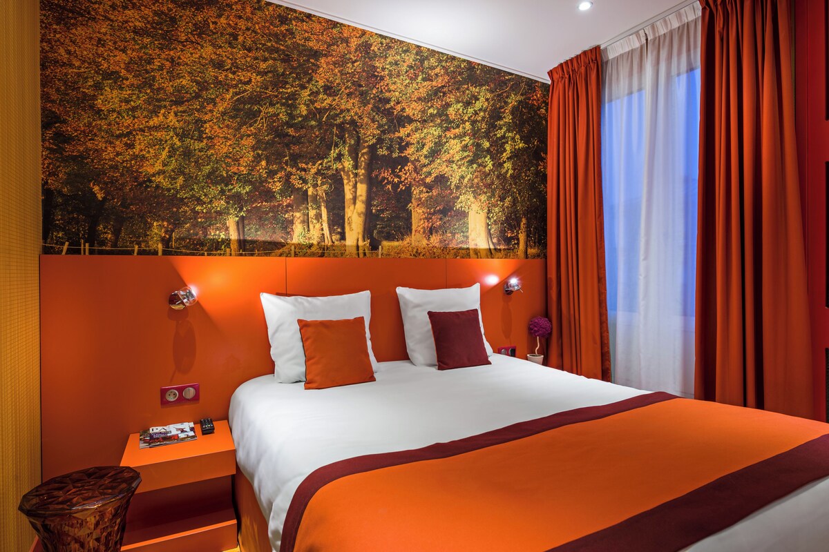 Una habitación de hotel con una cama grande, cortinas color naranja y un mural temático de bosque.