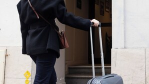 A woman in a red beret and dark coat exiting a hotel entrance with a suitcase. - Hotel Les Jardins de Montmartre (Paris)