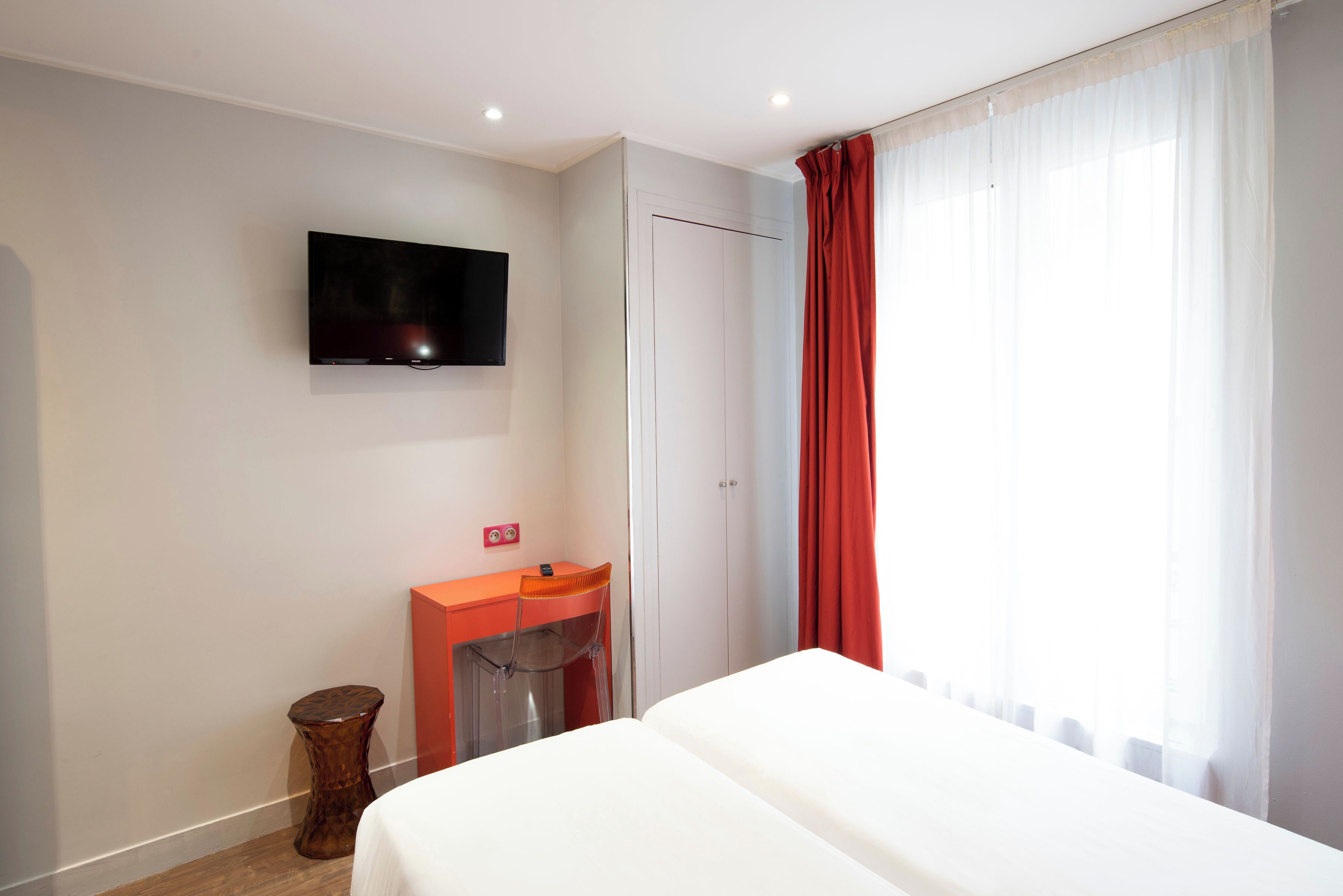 Een hotelkamer met een bed, een aan de muur bevestigde televisie, een bureau met stoel en een kledingkast.