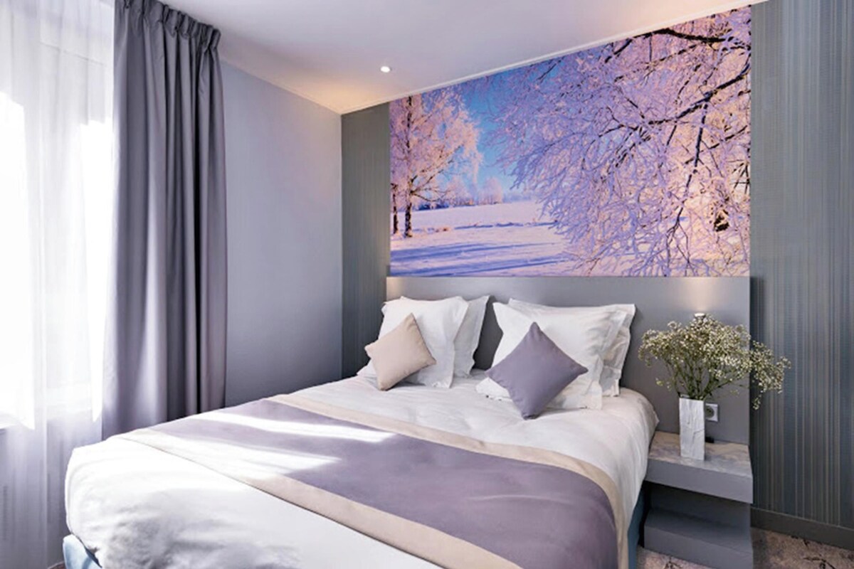 A modern bedroom with a large bed, a nightstand, and a wall-mounted painting of a winter landscape.
