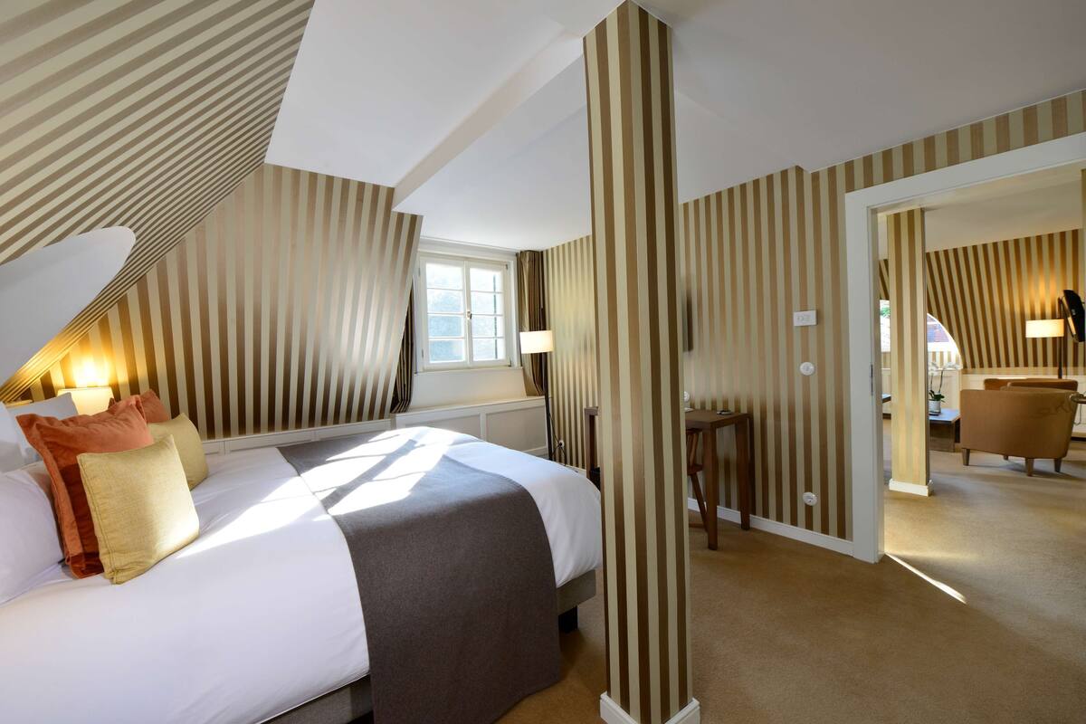 A hotel room with a large bed, striped wallpaper, a window, and a desk area.
