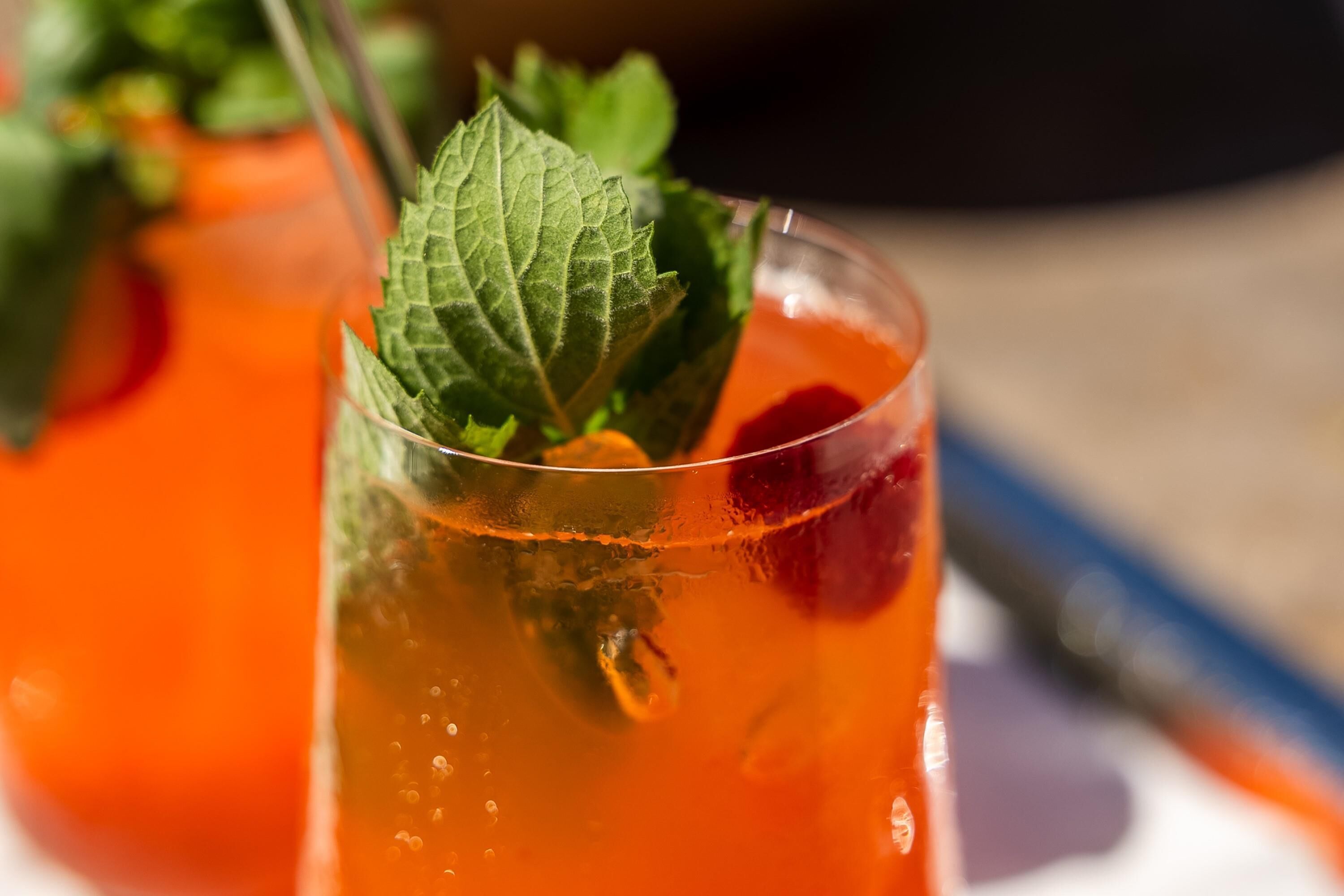 Un vaso de bebida de naranja con hojas de menta, posiblemente un cóctel, sobre una mesa.