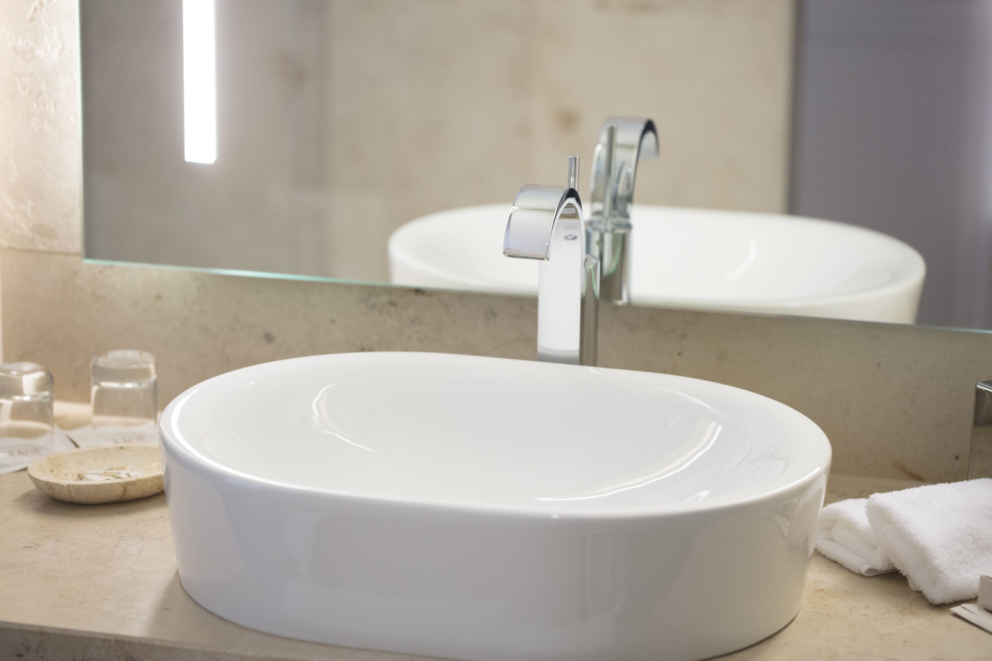 Ein weißes Keramikwaschbecken mit modernem Wasserhahn, einem Glastischchen und einem Spiegel darüber.