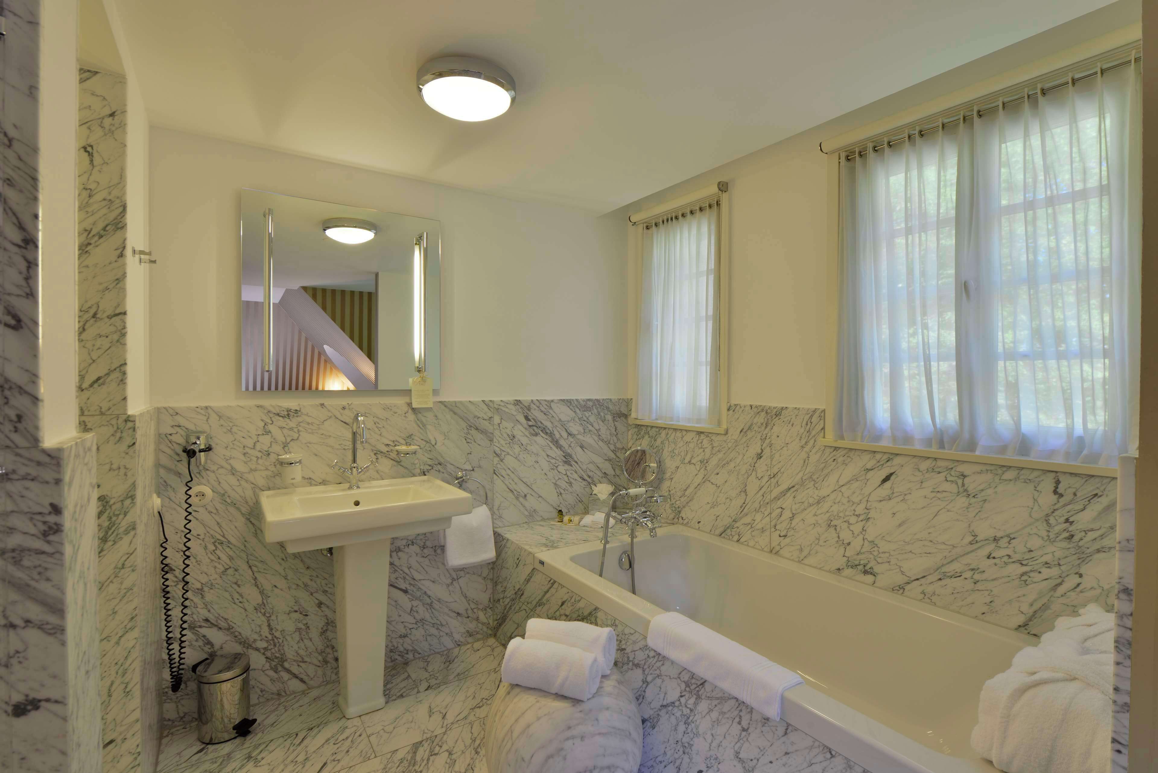 A bathroom with a marble floor, a sink, a bathtub, and a window with curtains.