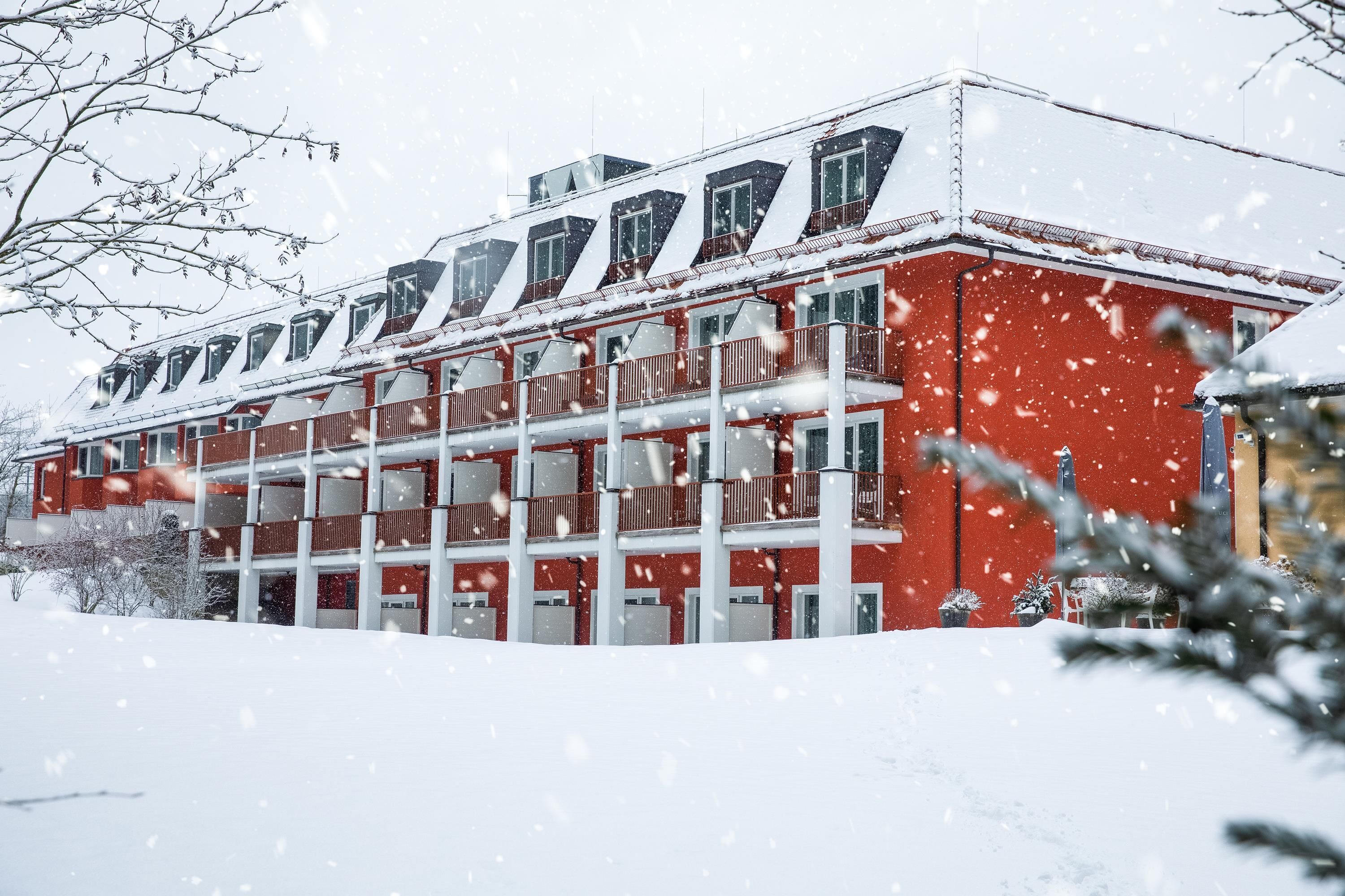 A red building with multiple balconies and a snow-covered roof.