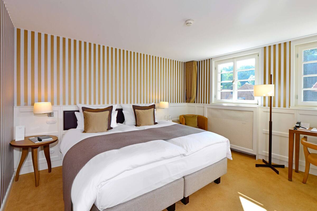 A hotel room with a large bed, bedside tables, a desk, and a window with curtains.