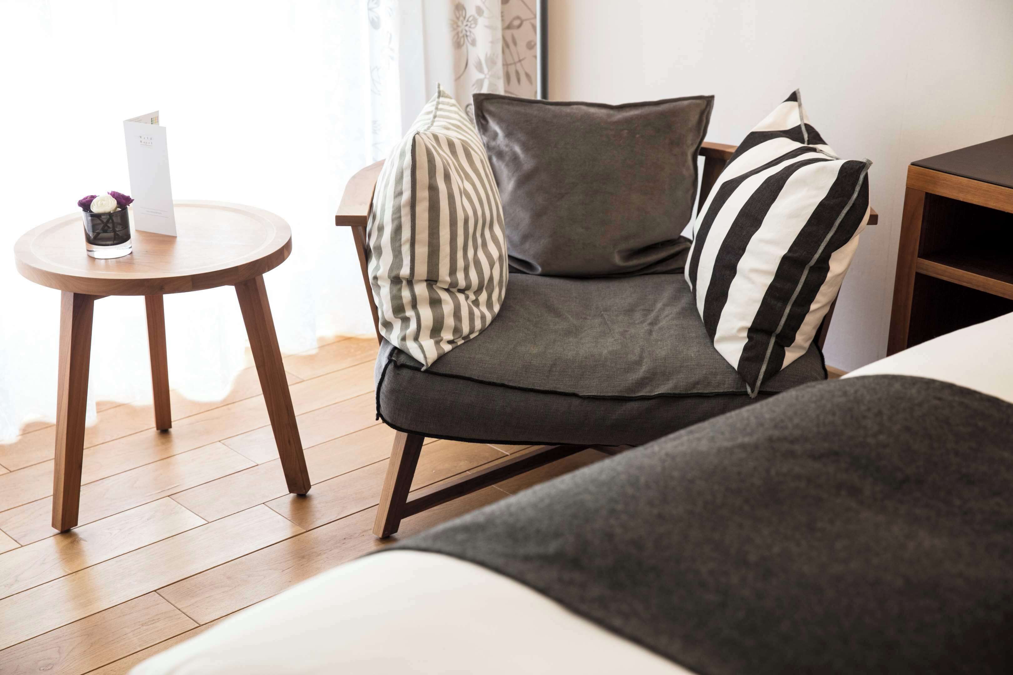 Una habitación de hotel moderna con un sofá gris, almohada a rayas y una pequeña mesa redonda con un menú.