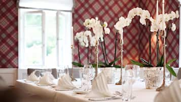 A dining table set with white napkins, glassware, and candles, with orchids in vases and a plaid-patterned wall in the background.