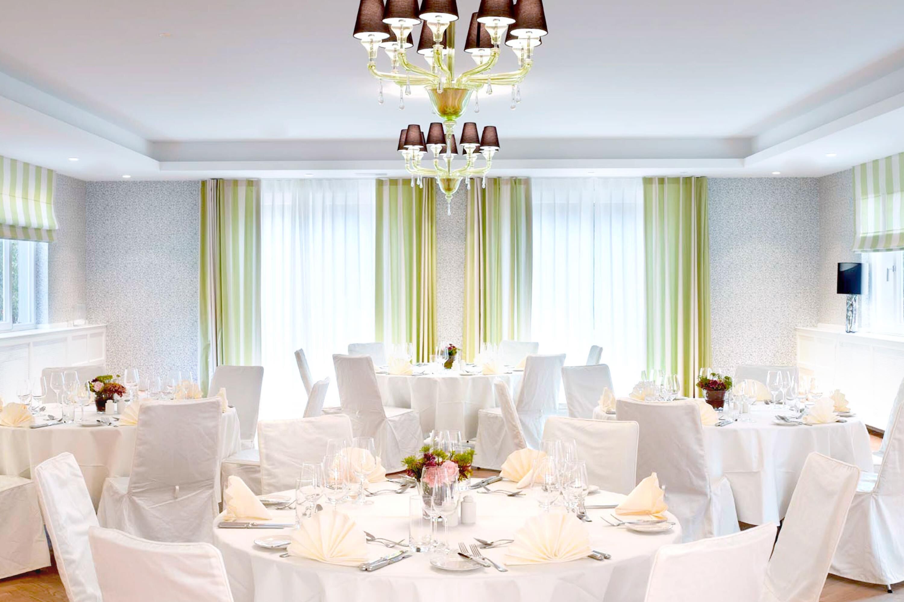 A formal dining room with round tables, white chairs, and a chandelier.