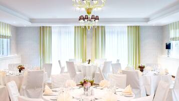 A formal dining room with round tables, white chairs, and a chandelier.