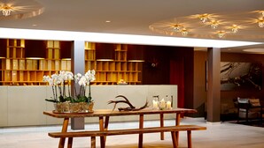 A wooden table with benches, a vase of white orchids, and decorative items in a modern lobby with a warm color scheme and ambient lighting.