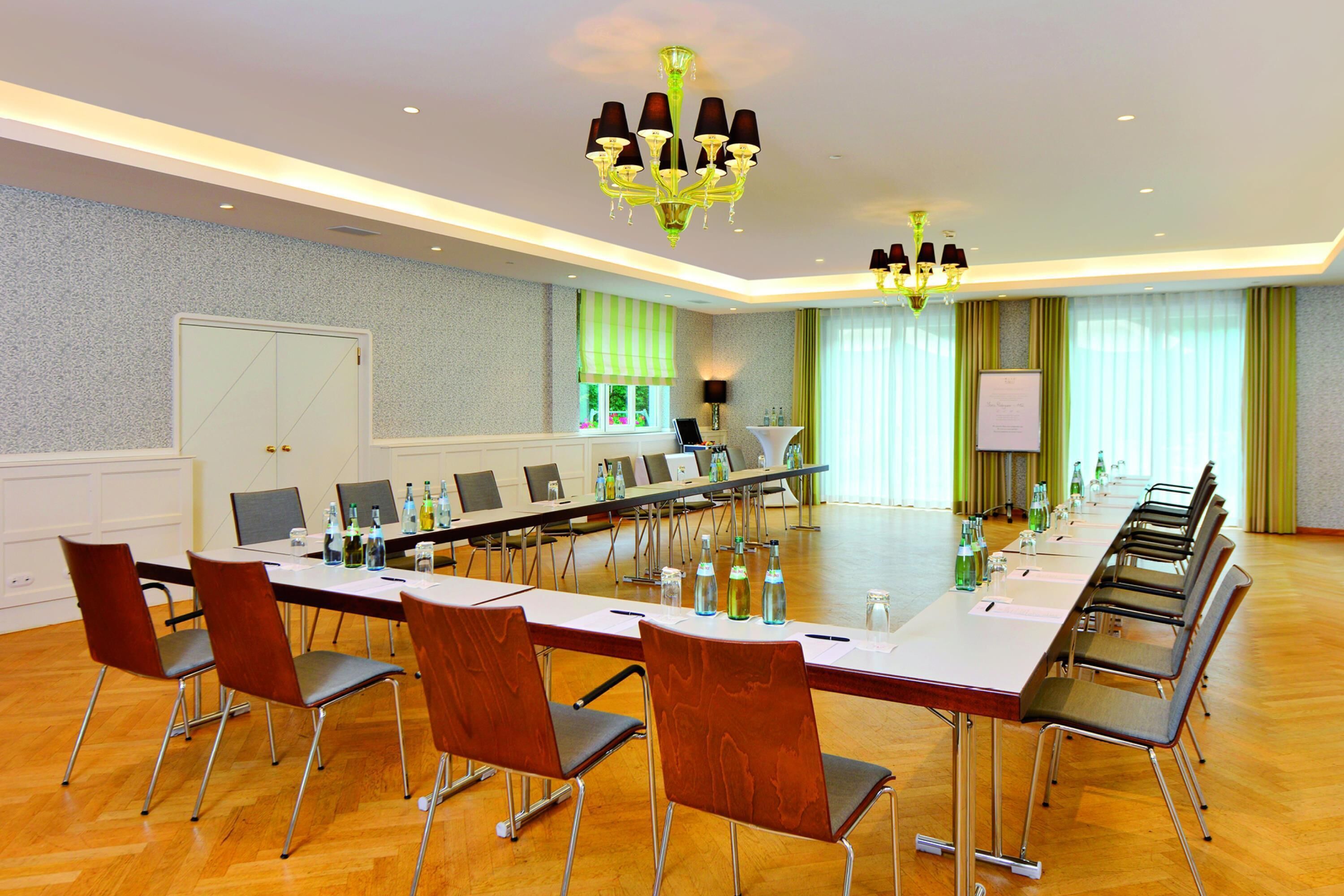 Ein Konferenzraum mit langem Tisch, Stühlen, einer Chandelüster und einer Whiteboard.