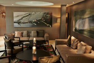 A modern living room with a sofa set, a coffee table, and two side tables. There are two large paintings on the walls, a floor lamp, and a decorative sun-like object on the left.