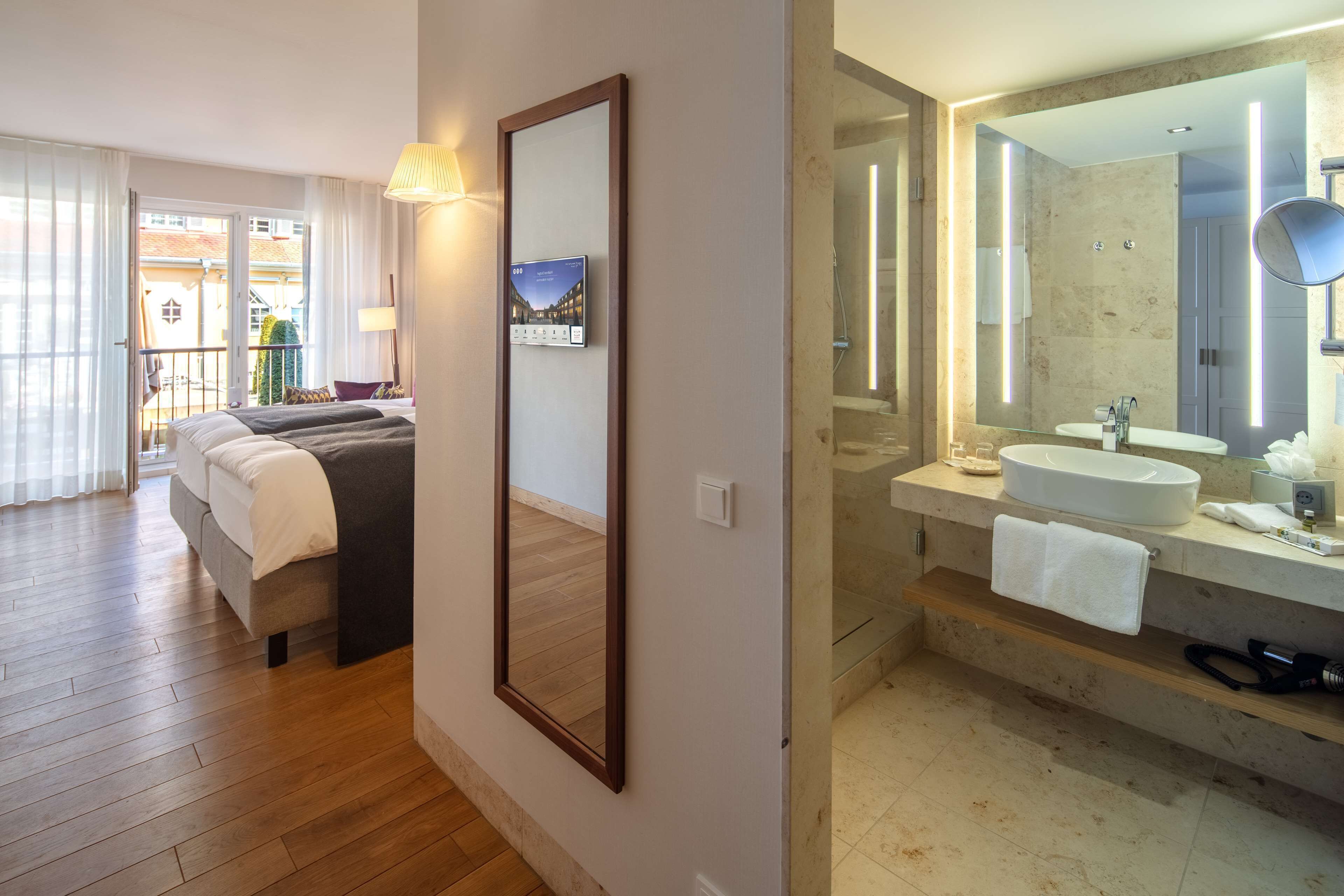Hotelkamer met een bed, een grote spiegel, een badkamer met een wastafel en spiegel, en uitzicht op het omliggende gebied.