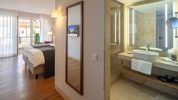 Hotelkamer met een bed, een grote spiegel, een badkamer met een wastafel en spiegel, en uitzicht op het omliggende gebied.
