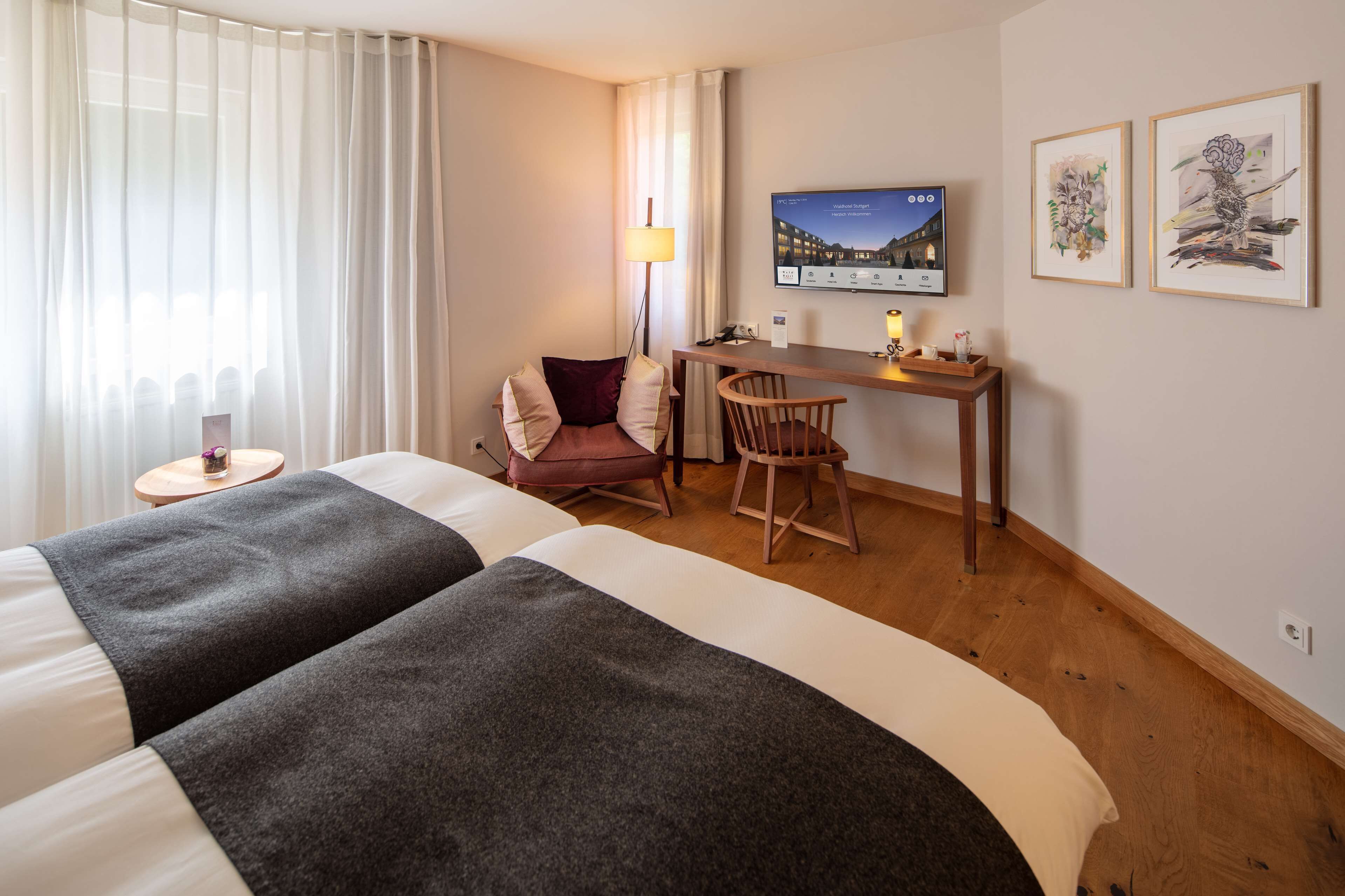 Ein Hotelzimmer mit zwei Betten, einem Schreibtisch, einem Stuhl, einem Fernseher und Bildern an der Wand.