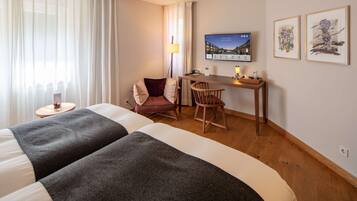 Ein Hotelzimmer mit zwei Betten, einem Schreibtisch, einem Stuhl, einem Fernseher und Bildern an der Wand.