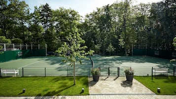 Una cancha de tenis rodeada de árboles, con bancos y plantas en macetas.