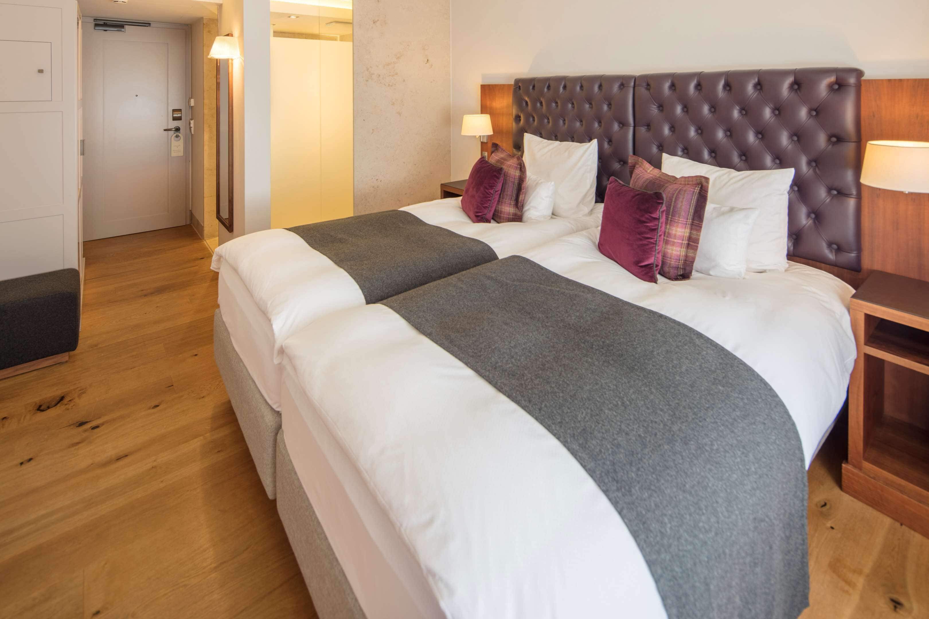 A double bed with a tufted headboard, two bedside tables with lamps, and a wooden floor.
