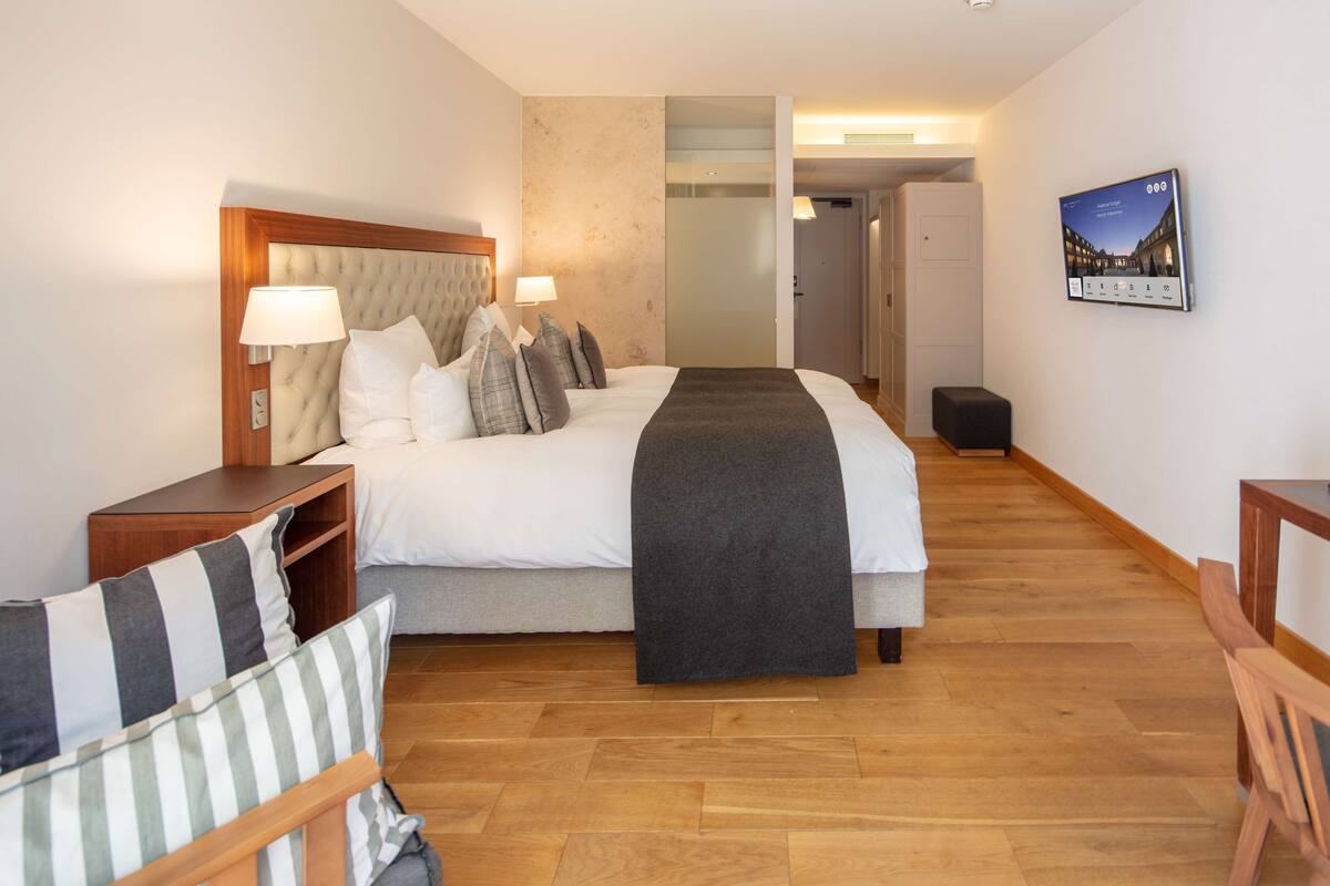 A hotel room with a large bed, wooden headboard, bedside tables, a chair, and a desk.