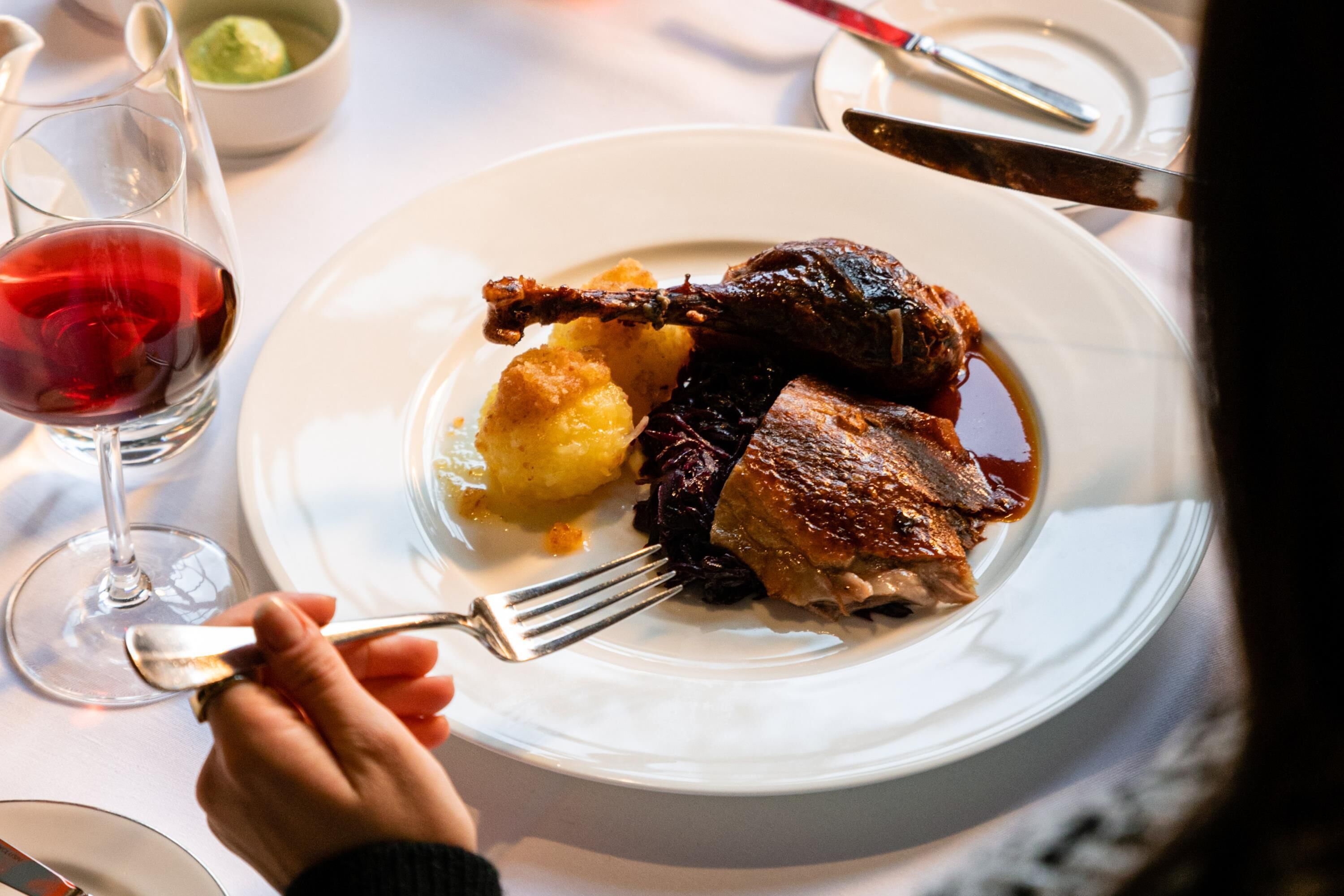 A dining table with a plate of food, a glass of red wine, and cutlery.