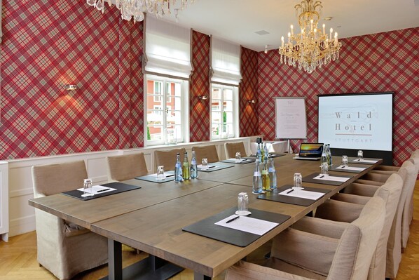 A conference room with a long table, chairs, and a projector screen displaying 'Wald Hotel'.