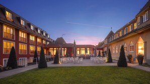 A courtyard with outdoor seating, a building with multiple windows and balconies, and a clear sky.