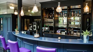 Un espace bar avec des chaises violettes, un comptoir avec une caisse enregistreuse et des étagères remplies de bouteilles et de verres.
