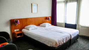 Una habitación de hotel con una cama grande, cabecera de madera, mesita de noche, lámpara y ventana con cortinas.