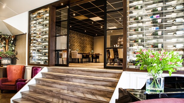 Un intérieur moderne avec un escalier menant à un espace repas, un meuble à vin et un coin salon agrémenté d’un vase de fleurs.