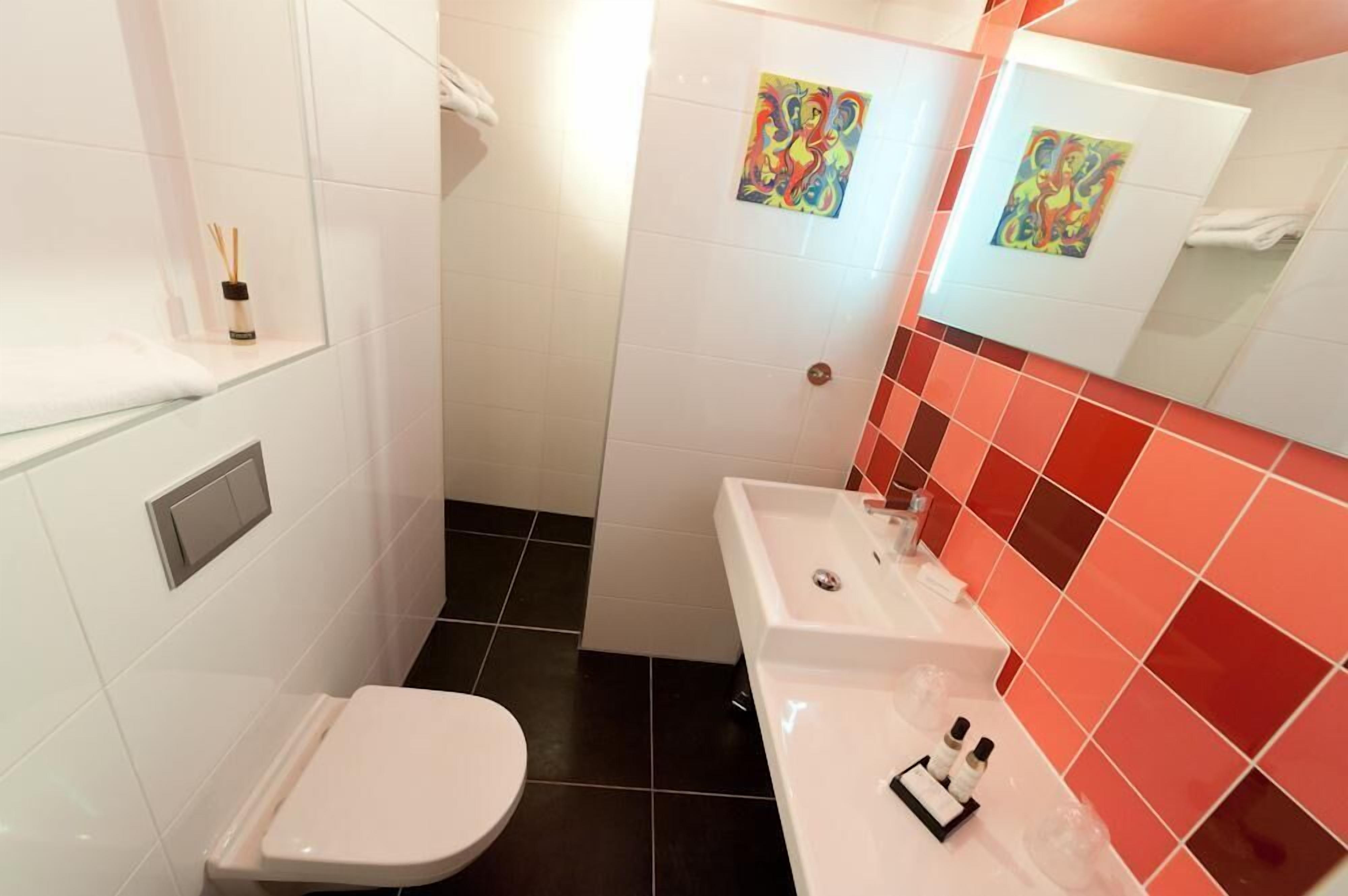 A bathroom with a white toilet, a sink with a mirror, and two colorful artwork pieces on the wall.
