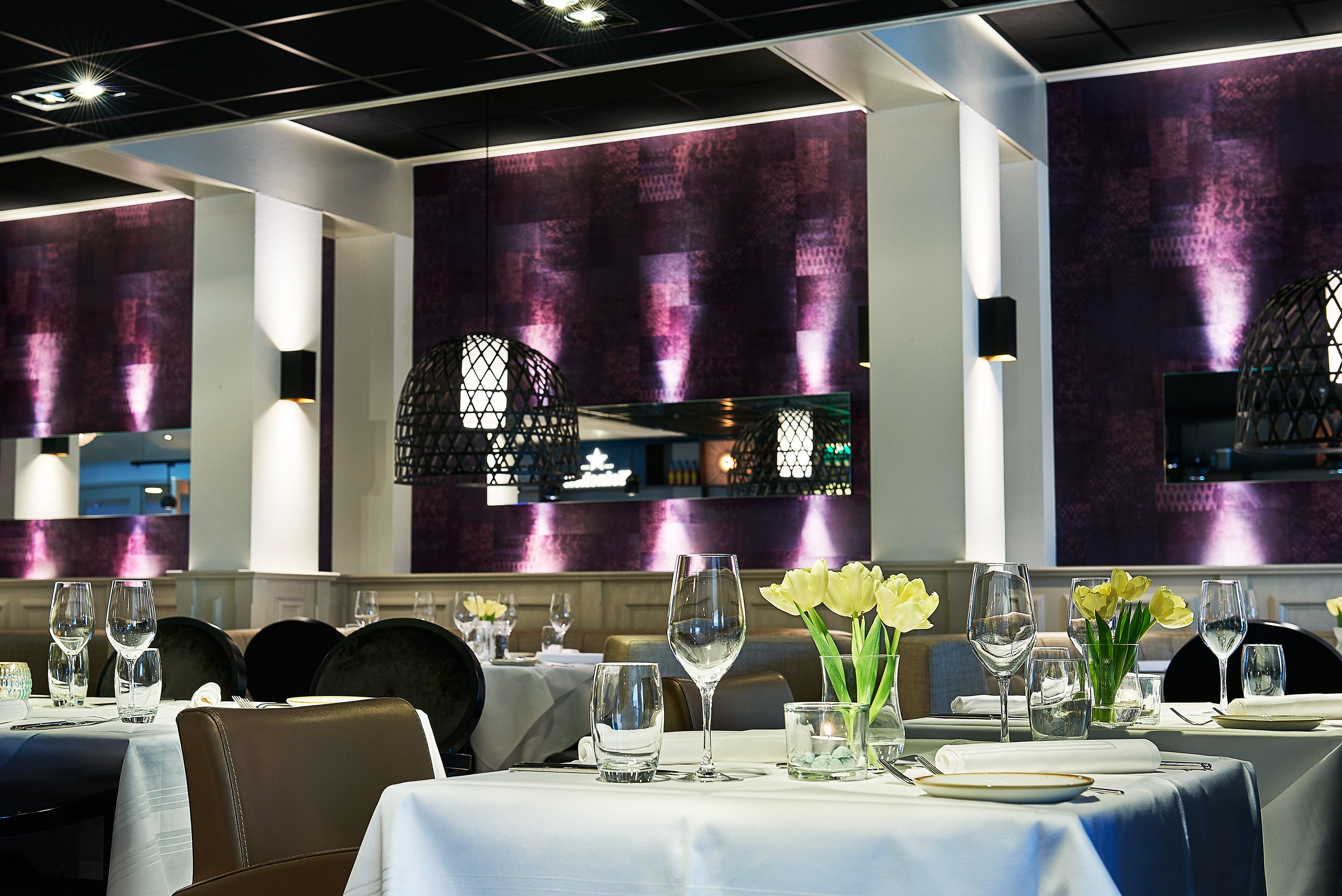 Un restaurante con mesas dispuestas para comer, con una decoración moderna que incluye paredes moradas y lámparas colgantes.