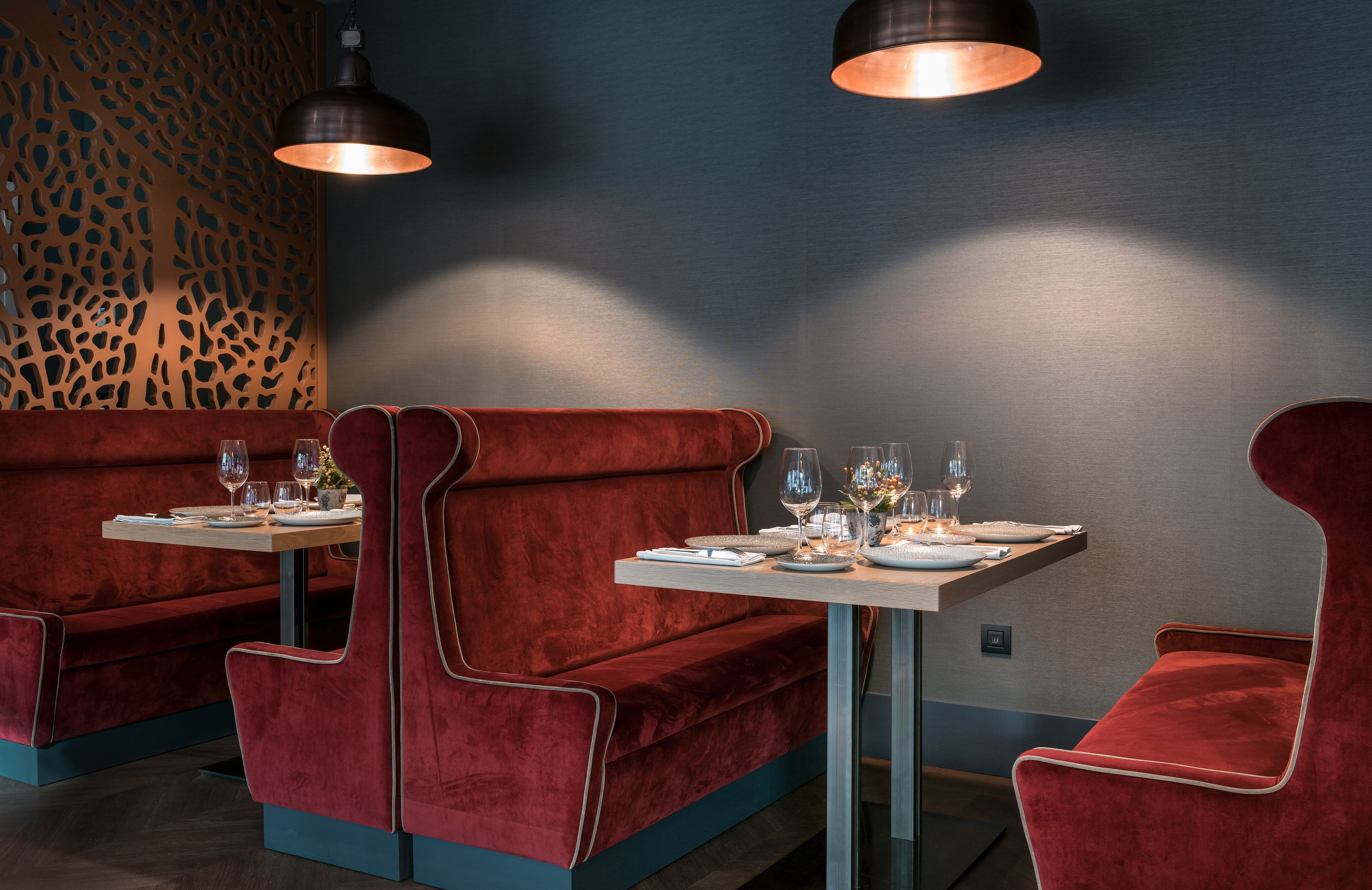 A restaurant with red velvet booths and tables, each with wine glasses and plates.