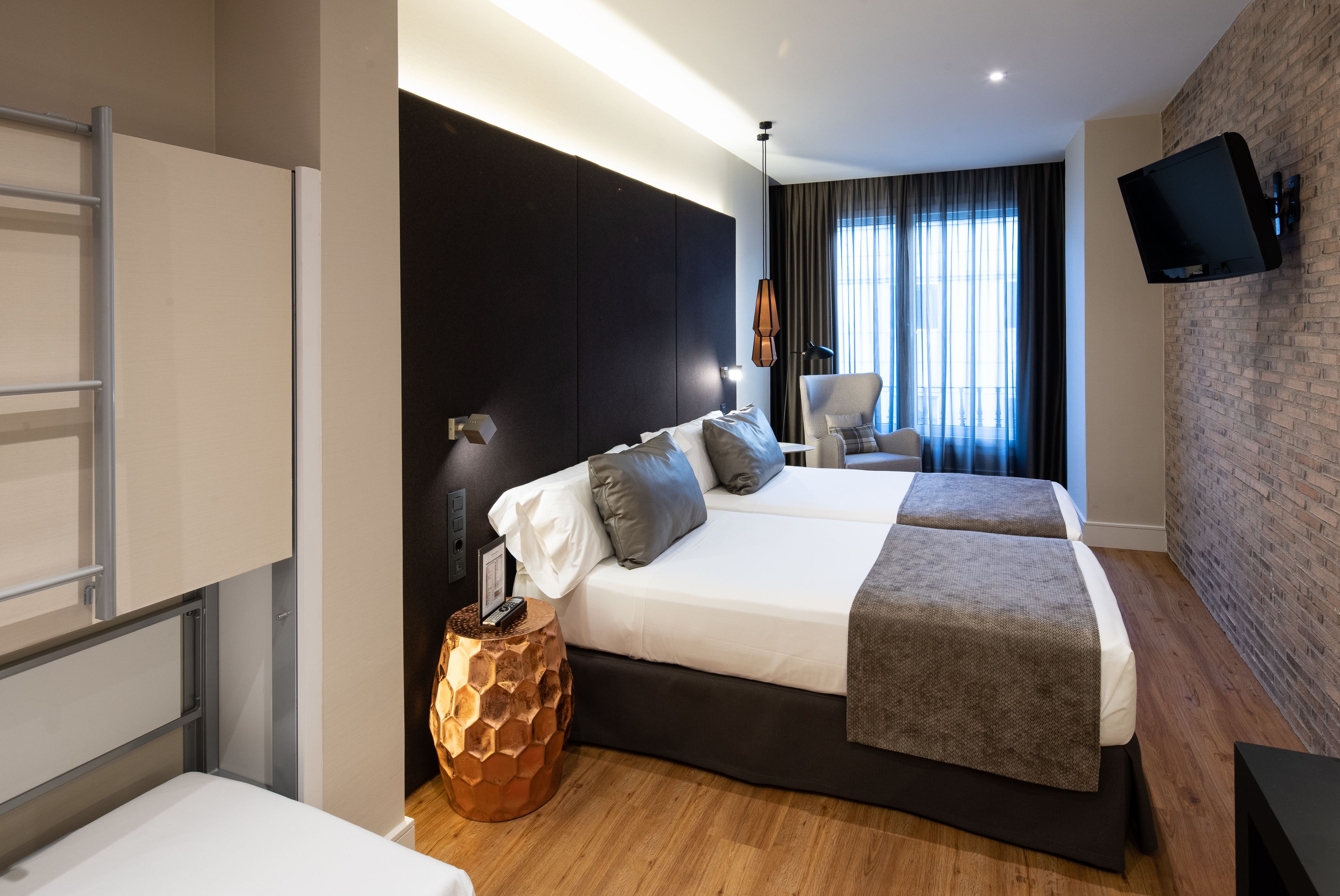 Ein modernes Hotelzimmer mit einem großen Bett, einem Schreibtisch, einem Stuhl, einem an der Wand montierten Fernseher und einem fenster mit Vorhängen.