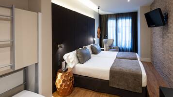 Ein modernes Hotelzimmer mit einem großen Bett, einem Schreibtisch, einem Stuhl, einem an der Wand montierten Fernseher und einem fenster mit Vorhängen.