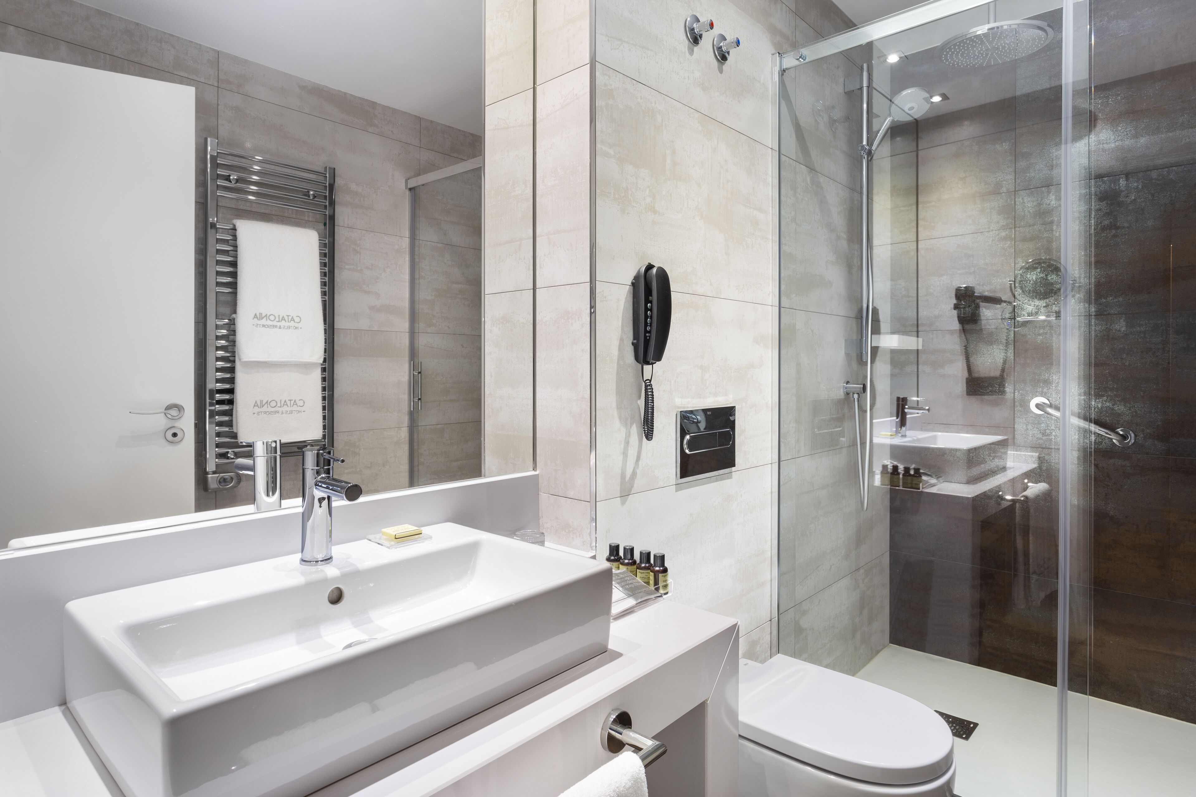 A modern bathroom with a large white sink, a glass-enclosed shower, and a toilet.