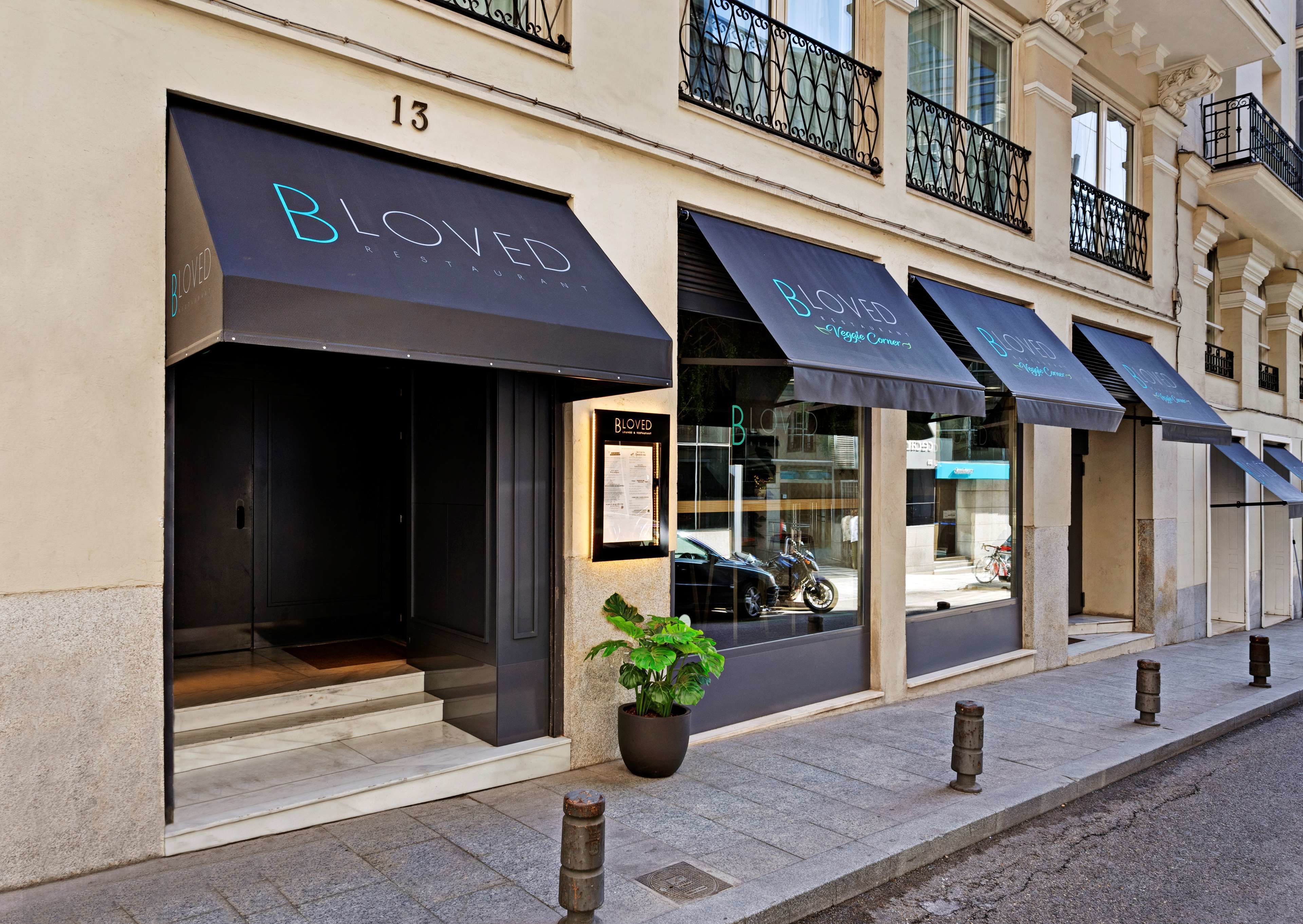 A building with multiple storefronts, including a restaurant named "Bloved" with a modern design and a potted plant in front.