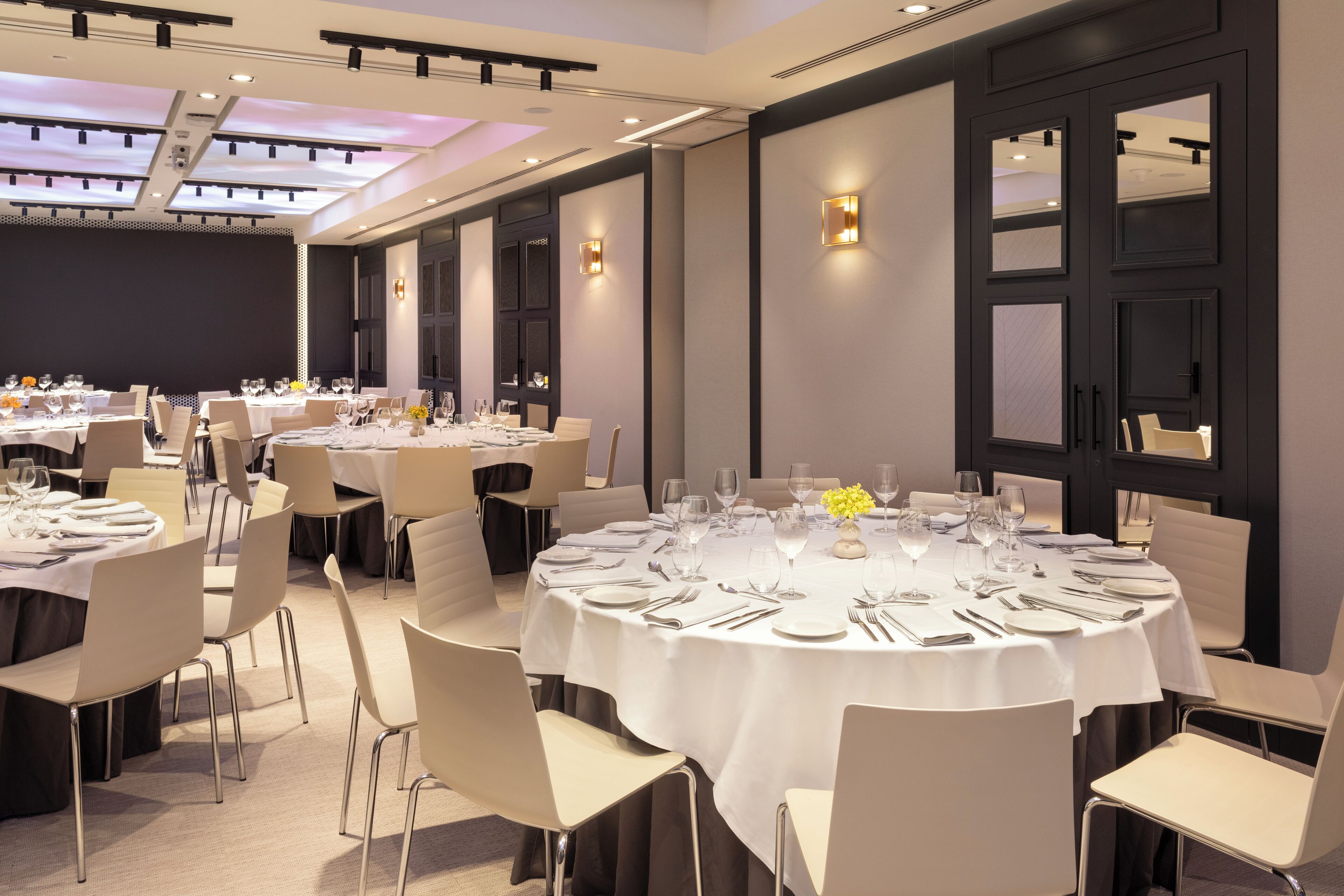 A conference room with multiple round tables set for dining, equipped with chairs and table settings.