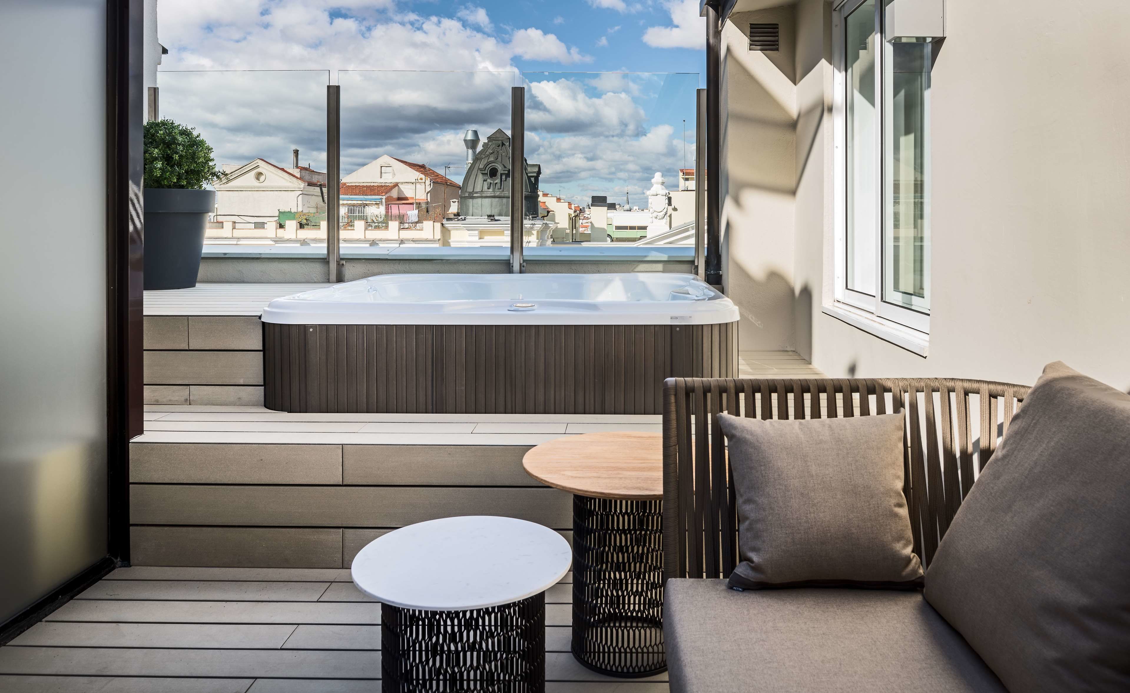 A balcony with a hot tub, a round table, and a cushioned chair.