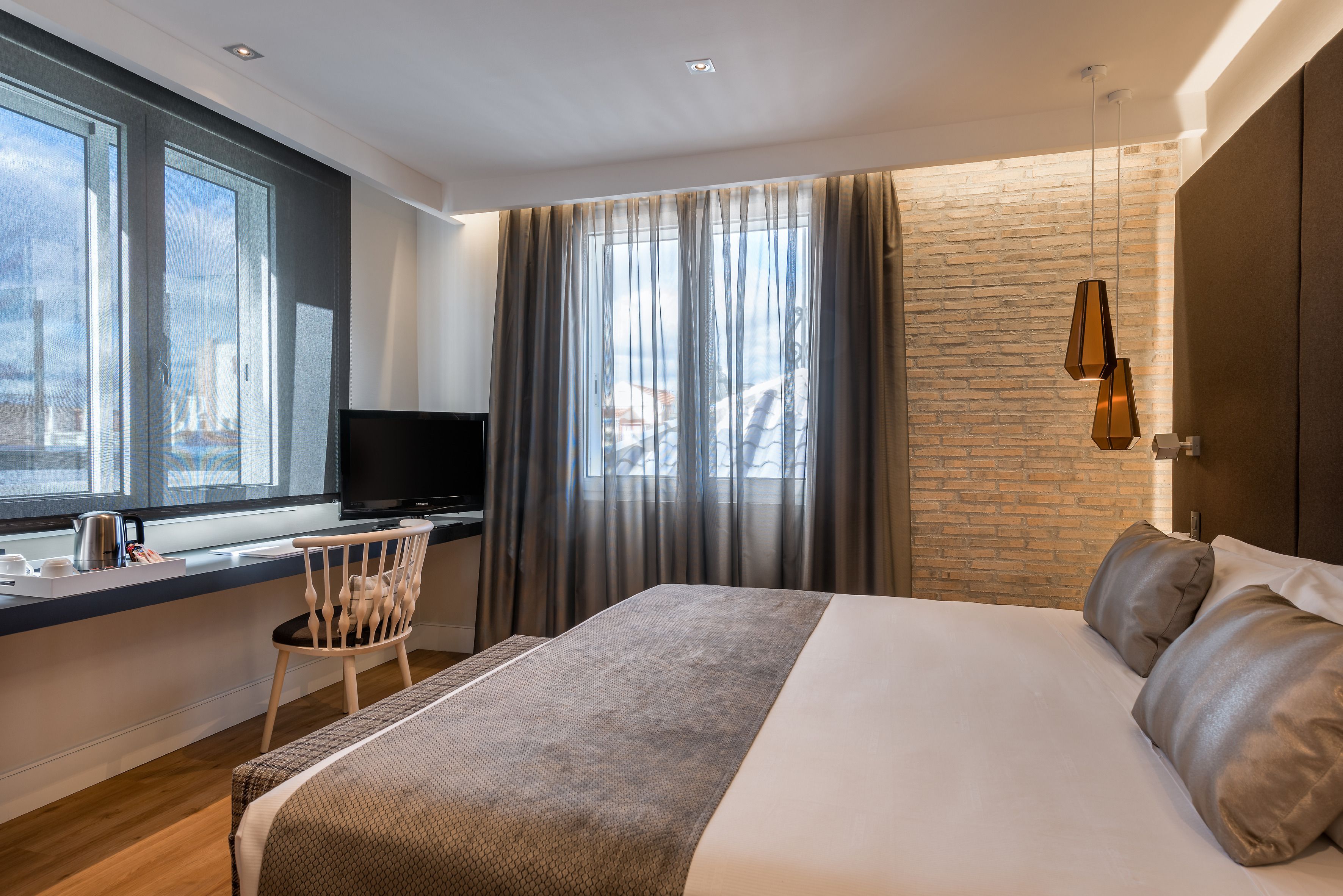 Ein modernes Hotelzimmer mit einem großen Bett, einem Schreibtisch mit Fernseher und Blick auf die Stadt durch große Fenster.