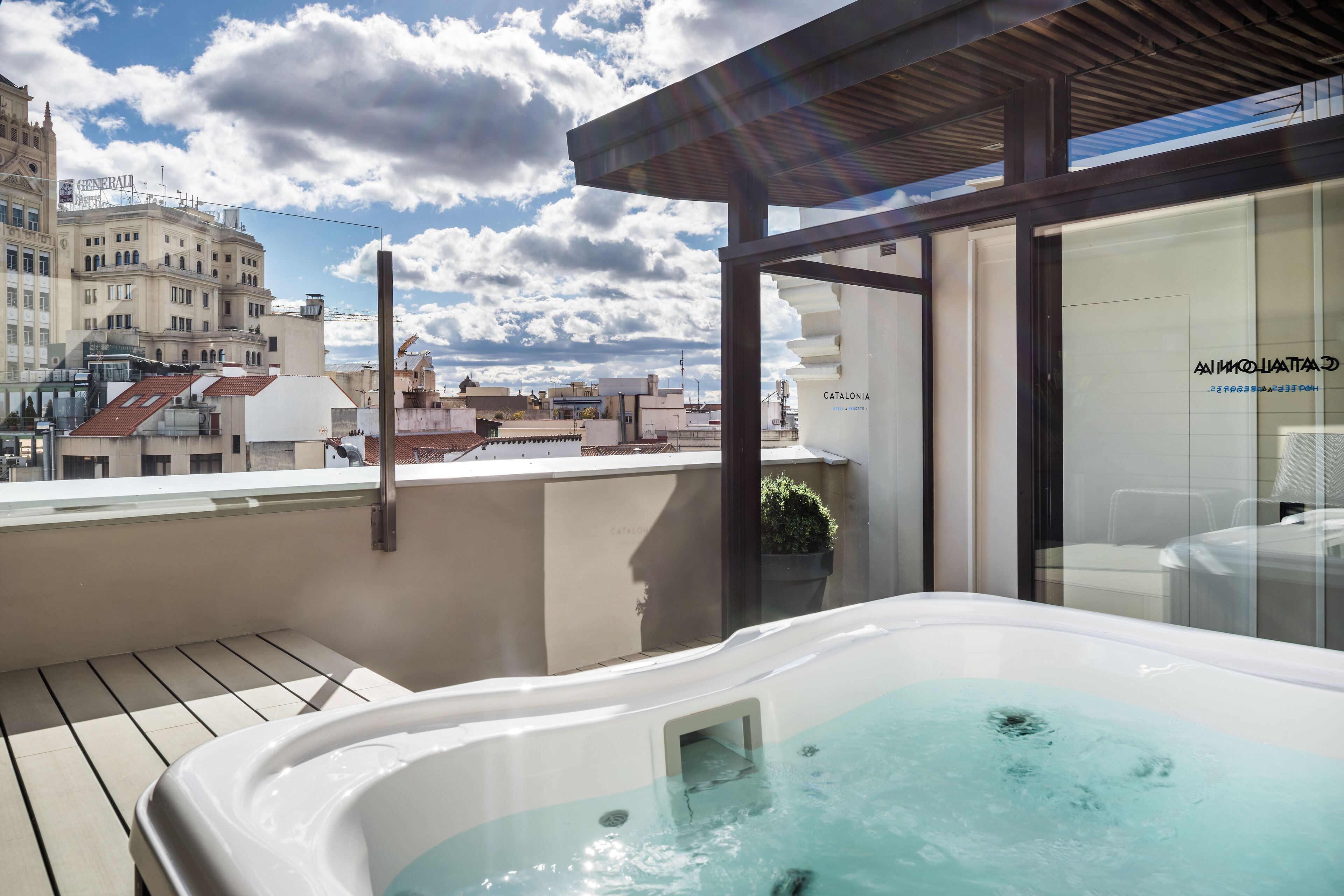 Terraza en la azotea con un jacuzzi, una puerta de cristal con el letrero 'Catalonia' y vistas panorámicas de la ciudad.