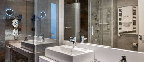 A modern bathroom with a large mirror, two sinks, a shower, and a towel rack.