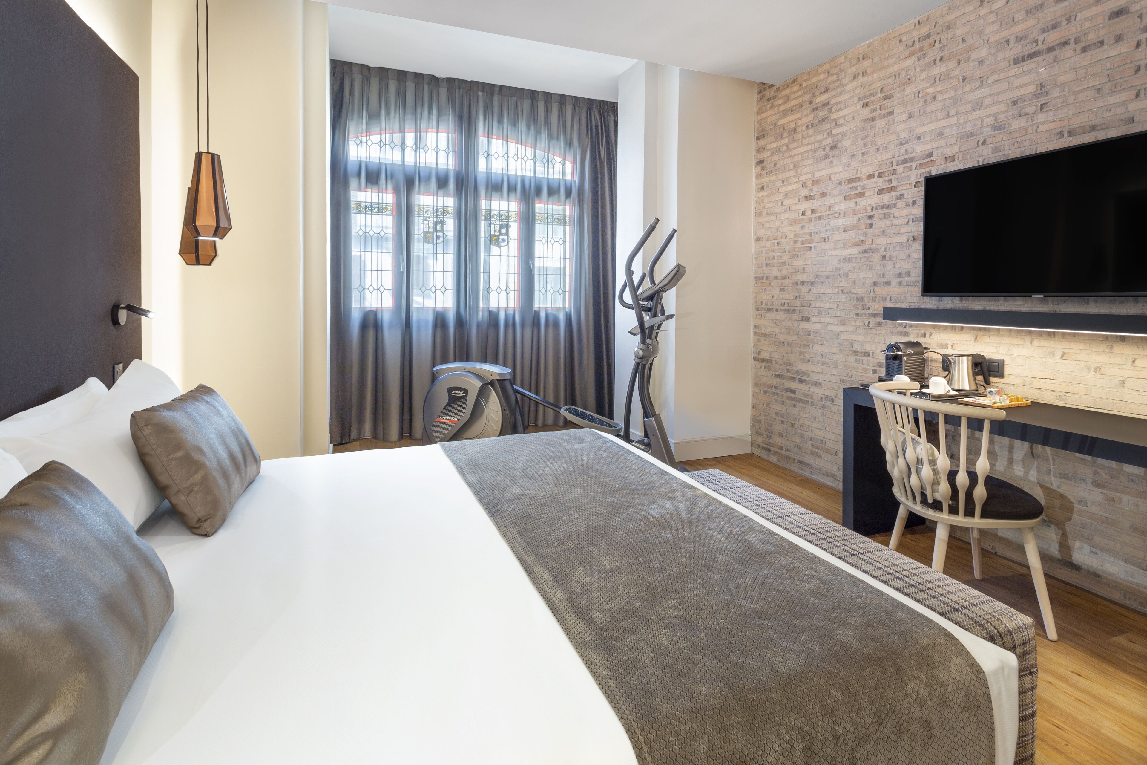 A hotel room with a large bed, a desk with a chair, a television mounted on the wall, and a window with curtains.