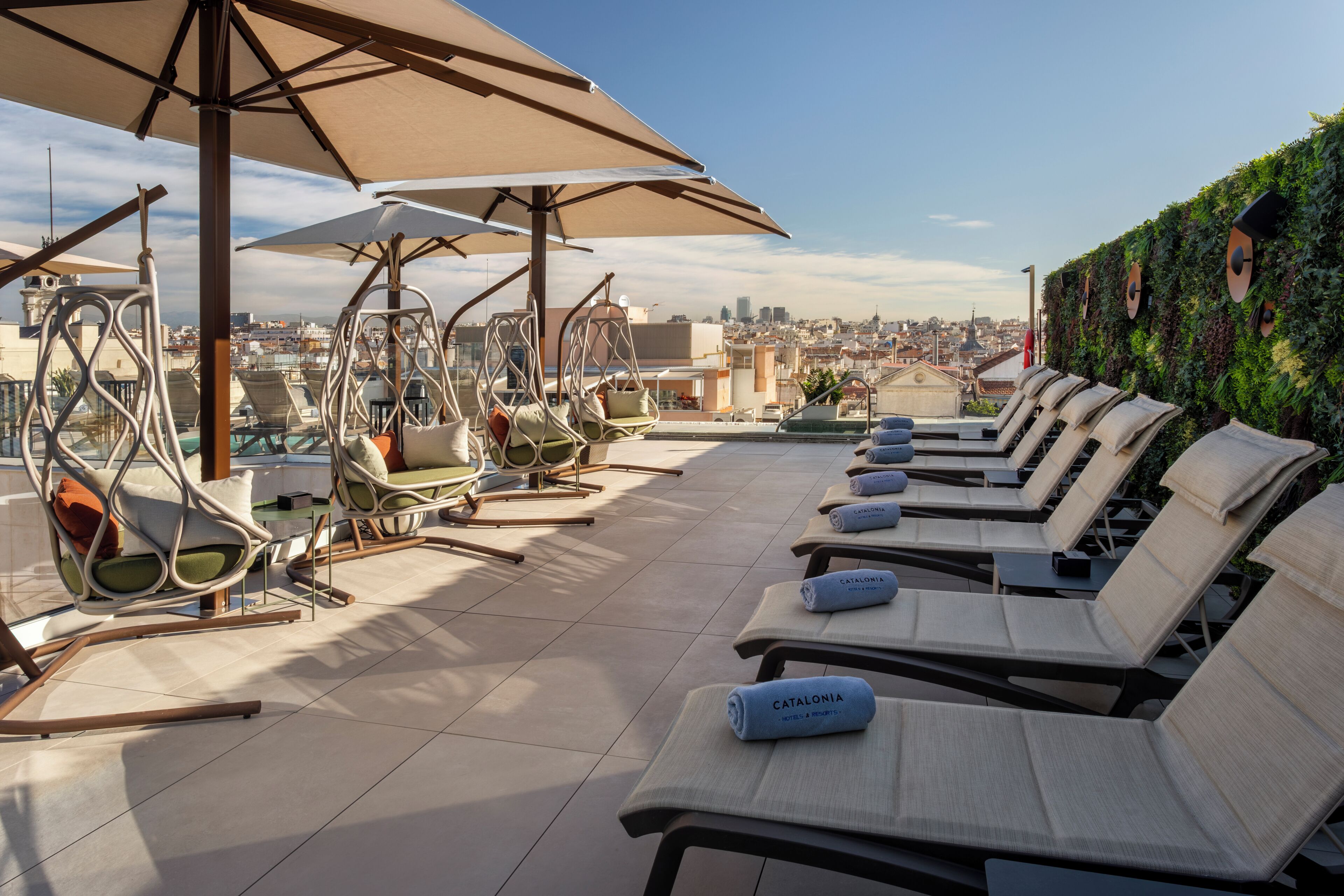 A rooftop terrace with lounge chairs, umbrellas, and a city view.