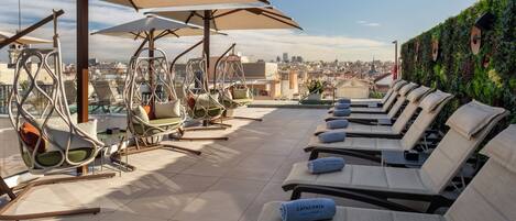 Terraza en la azotea con sillones de descanso, sombrillas y vista a la ciudad.