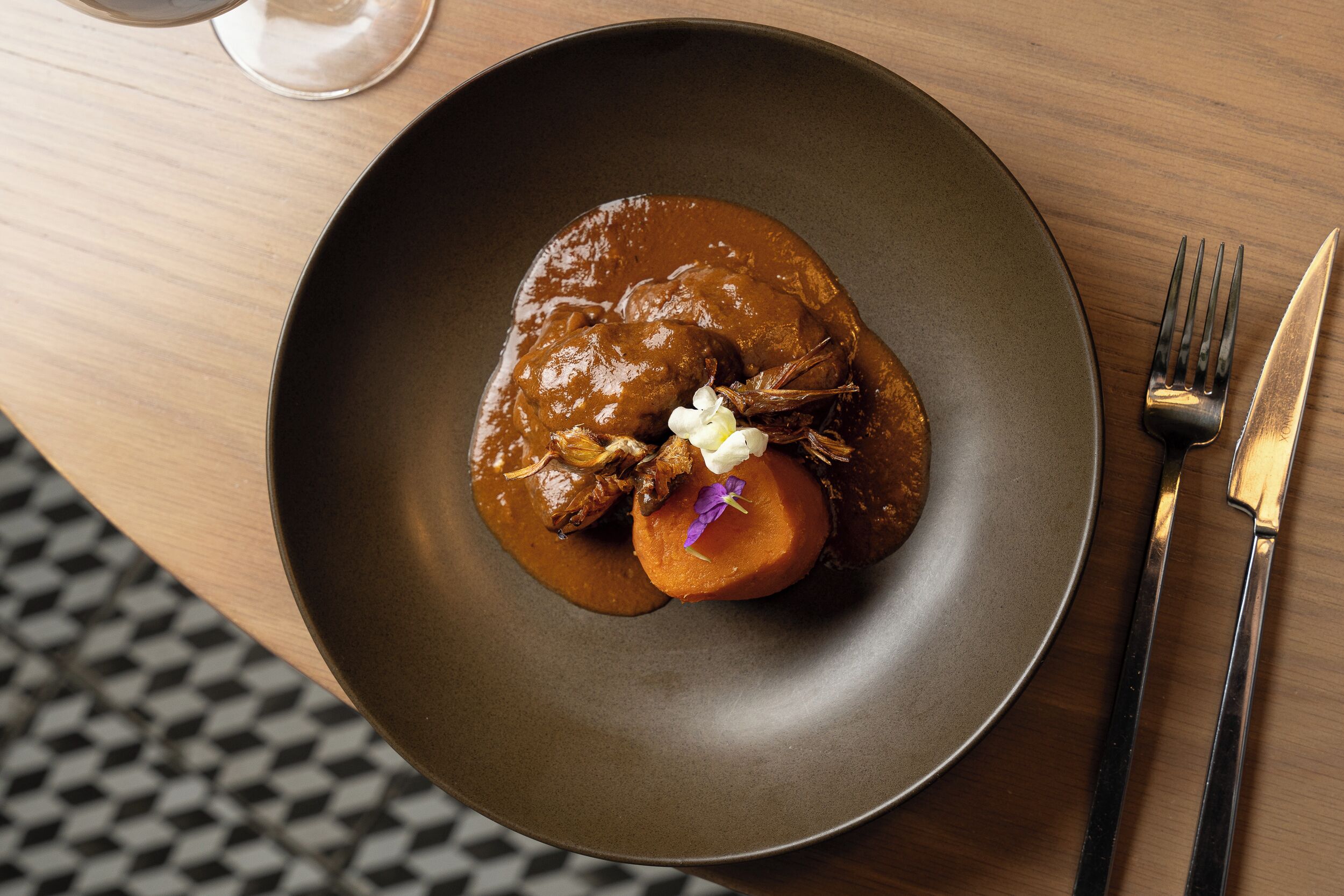 A plate of food with a dark sauce, garnished with flowers, on a wooden table.