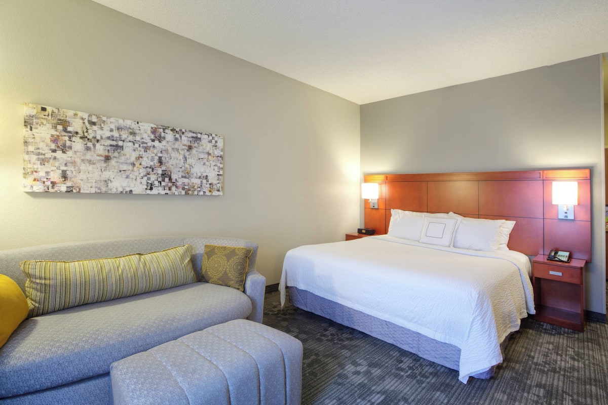 A hotel room with a bed, a sofa, a nightstand, and a wall-mounted artwork.