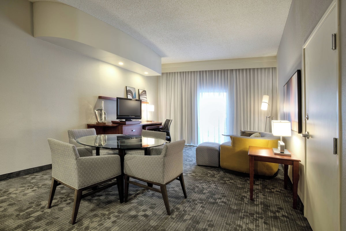 A hotel room with a round dining table, four chairs, a sofa, a TV, and a lamp.