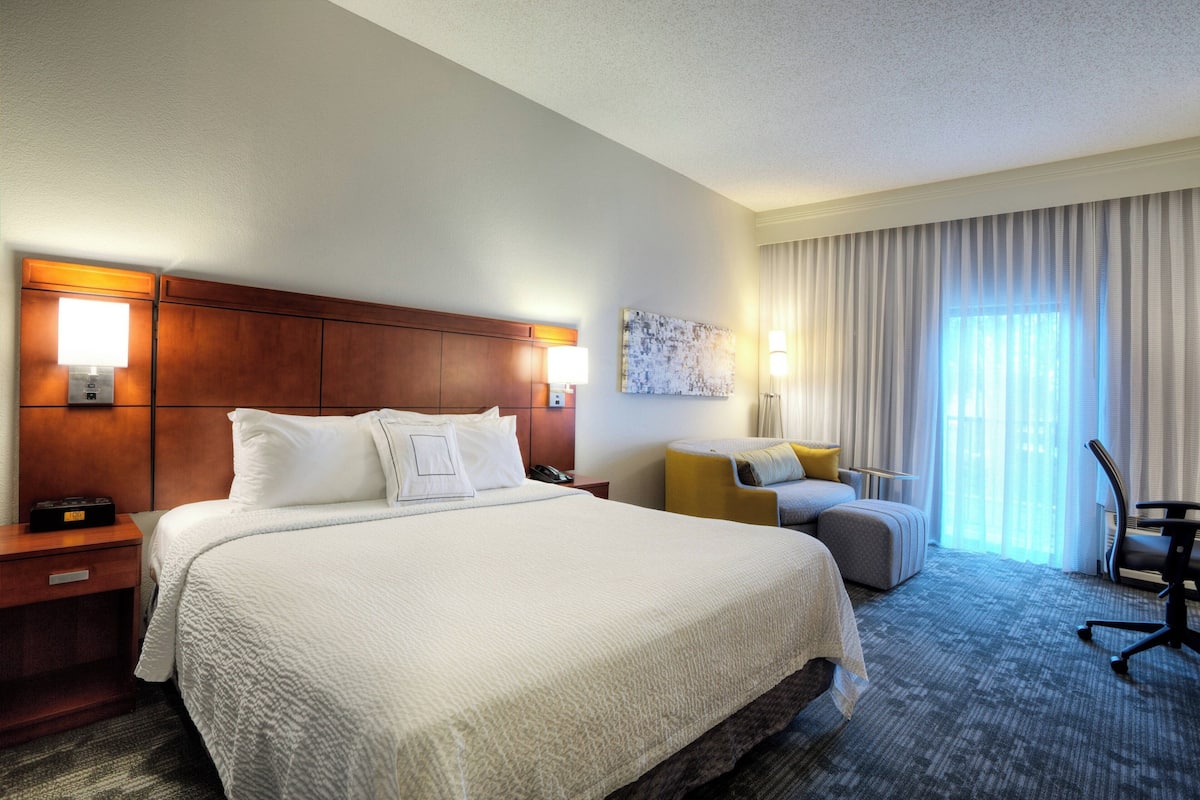 A hotel room with a large bed, a desk, a chair, and a window with curtains.
